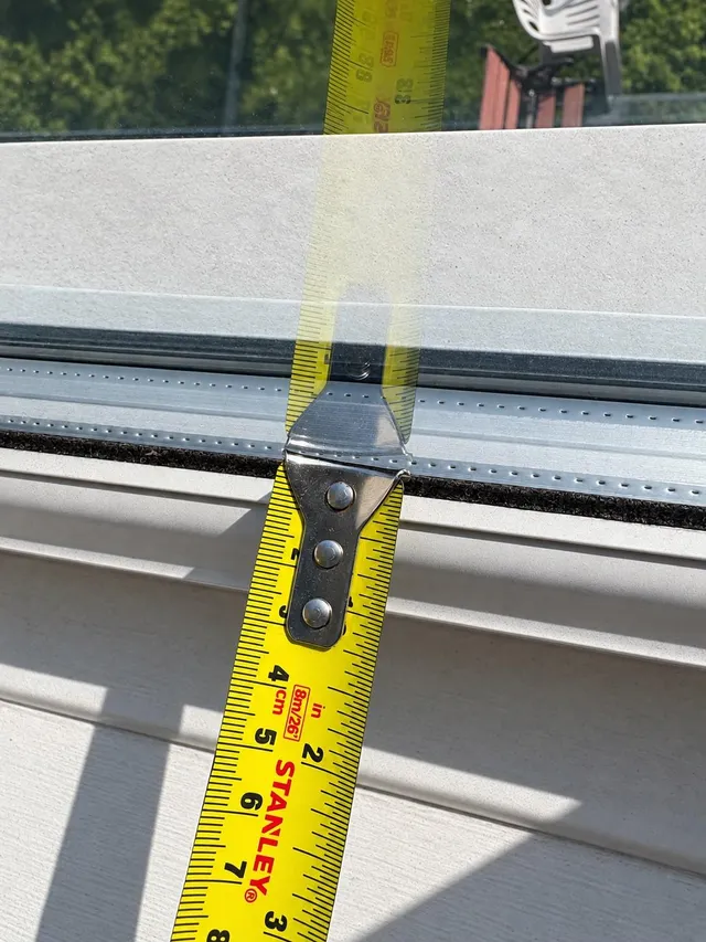 A tape measure held against the edge of a double-glazed unit to measure the gap between the panes.